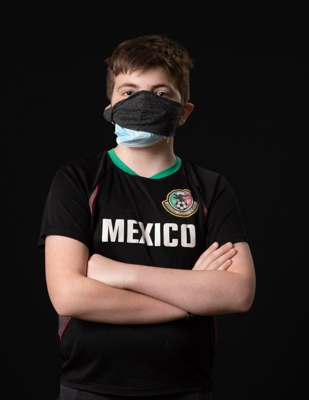 photo of young person in face mask and black 'Mexico' t-shirt with arms crossed
