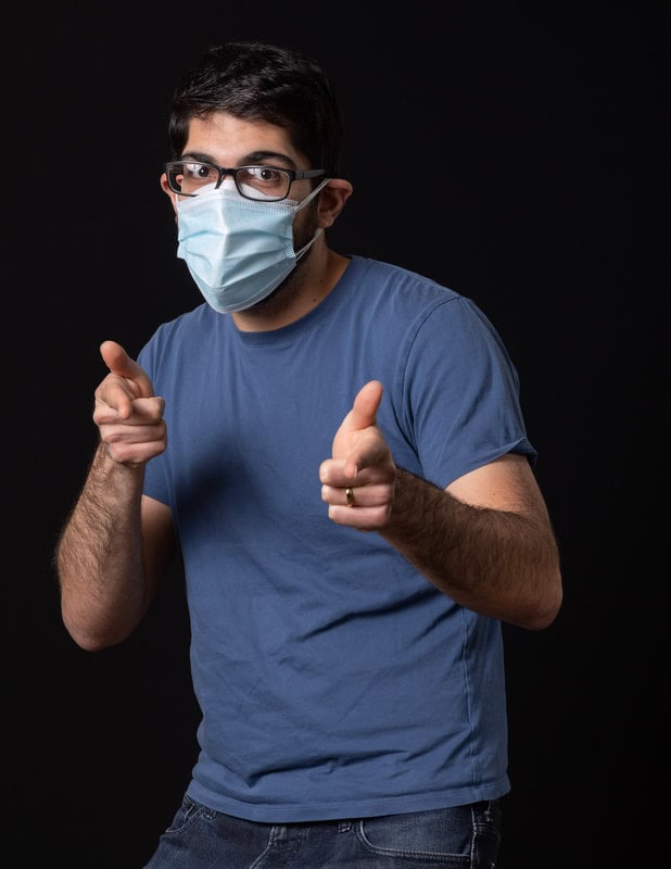 Photo of person wearing face mask and pointing two fingers at camera