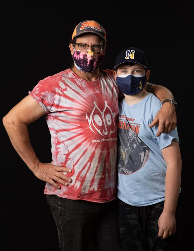photo of older person with arm around younger person wearing face masks and t-shirts
