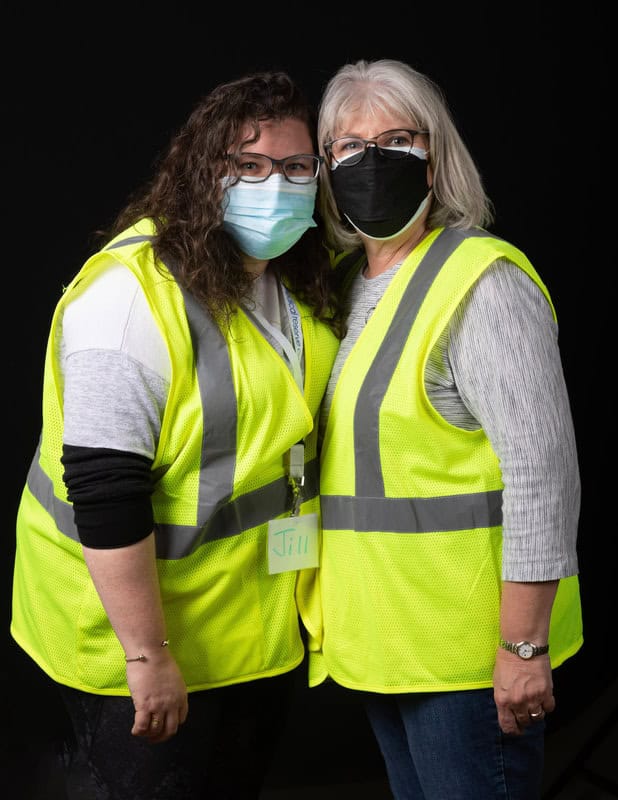 photo of two people hugging each other, wearing face masks and yellow vests