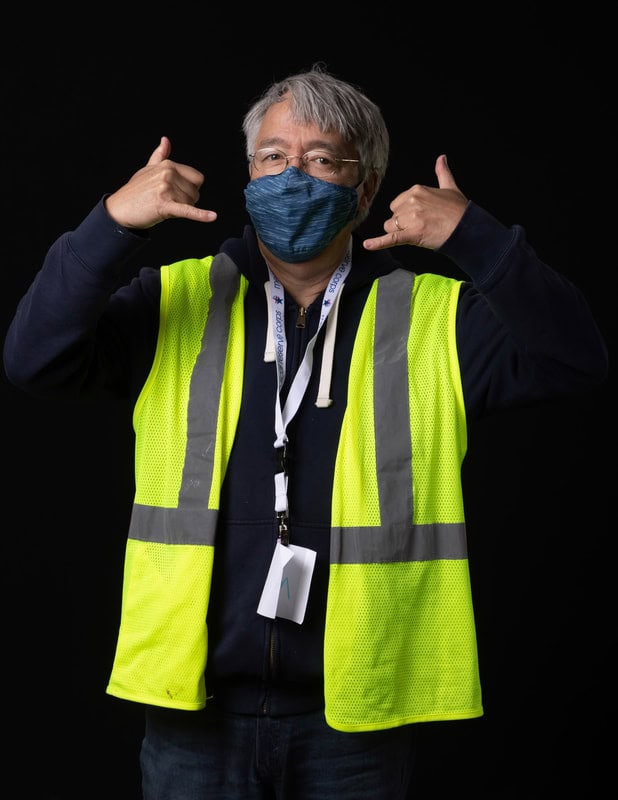 Photo of person wearing face mask and yellow vest holding up two hands in gesture