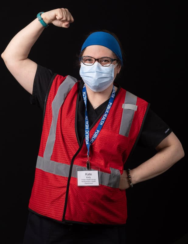 photo of person in face mask wearing a red vest and lanyard with raised arm showing muscle