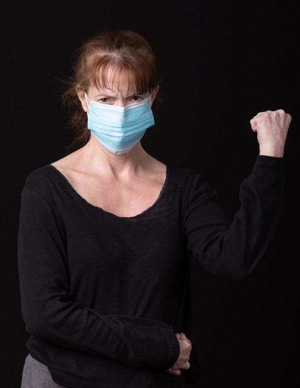 photo of woman wearing face mask and black shirt with angry eyes and fist raised