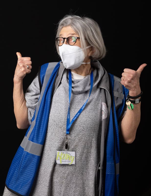 photo of person in face mask wearing a blue vest and lanyard with two thumbs up