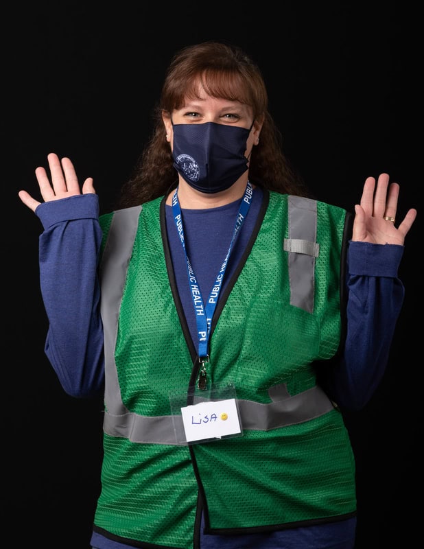 photo of person wearing face mask and green vest holding both hands up