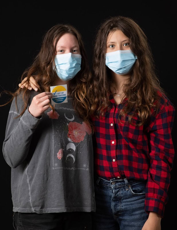 photo of two young people wearing face masks, one holding up an 'I got my covid vaccine' sticker