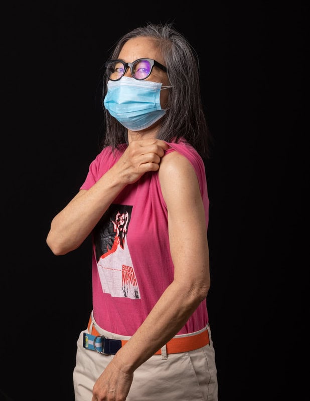 photo of woman wearing face mask and pink shirt, pulling up sleeve on one arm