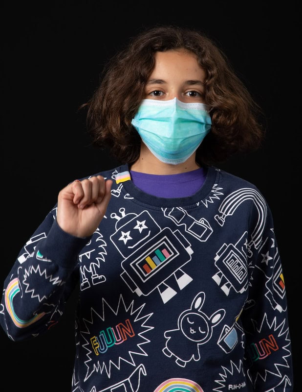 photo of young person wearing face mask and blue illustrated sweater with fist raised