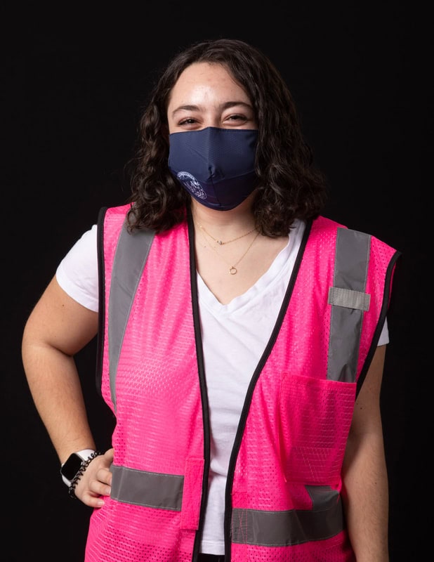 photo of person wearing face mask and a pink vest with one hand on hips