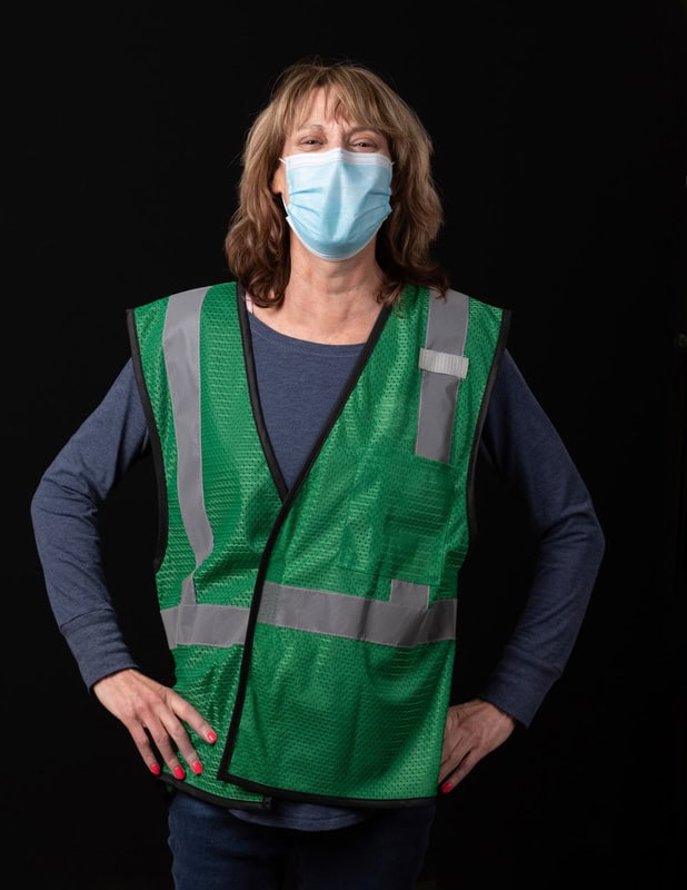 photo of person wearing face mask and green vest with hands on hips