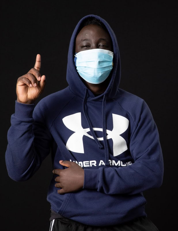 photo of young person wearing face mask and hooded sweatshirt holding up one finger