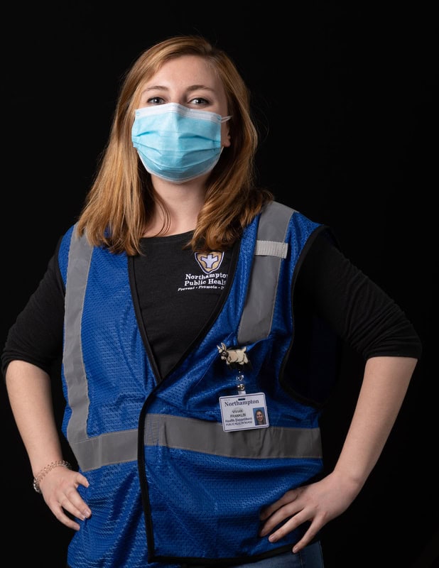 photo of person in face mask wearing a blue vest with hands on hips