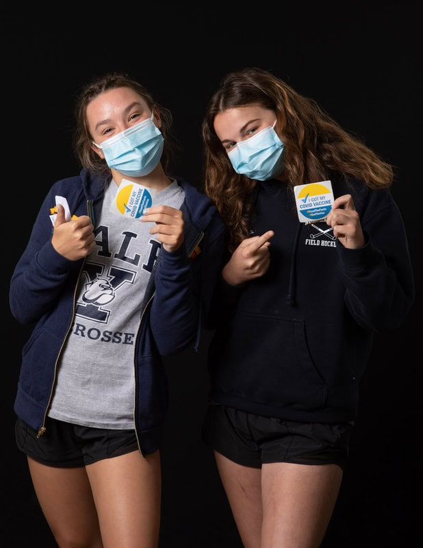 photo of two young people wearing face masks, one giving thumbs up and both holding 'I got my Covid vaccine' stickers